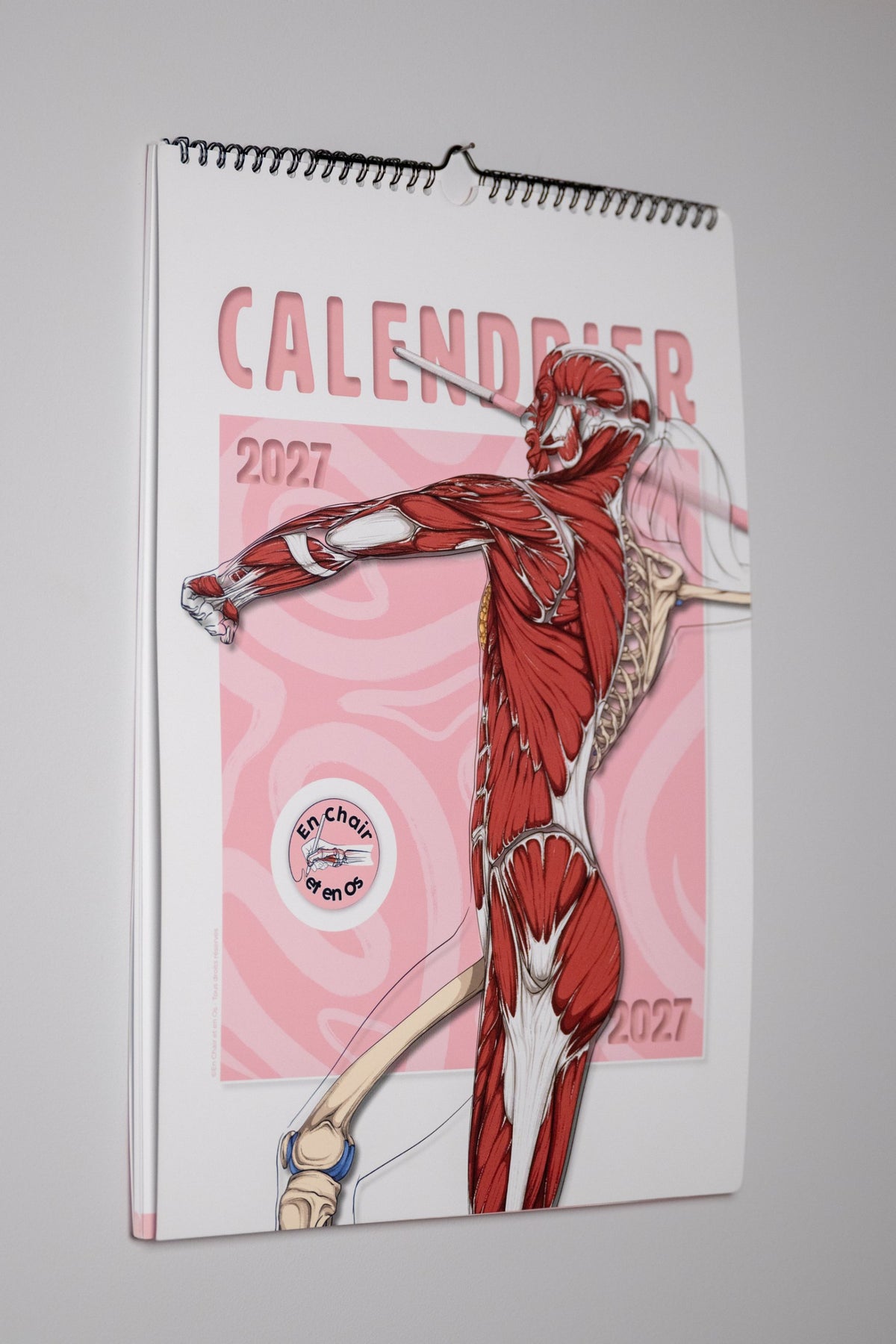 Calendrier mural A3 2027 En Chair et en Os accroché au mur, reliure spirale noire